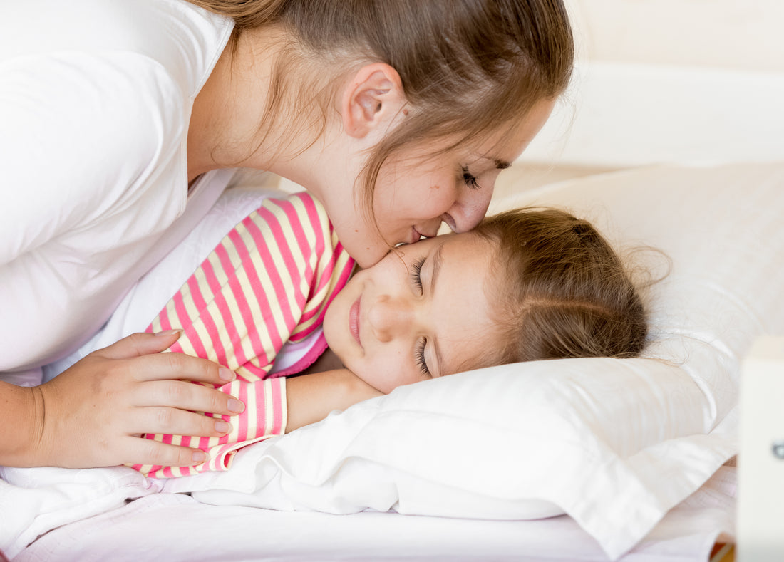 Mom kisses elementary-aged girl goodnight after creating a soothing bedtime routine.    
